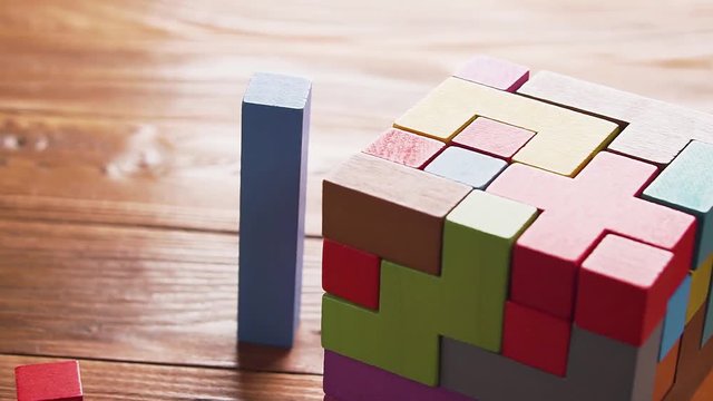 Hand folds colorful wooden cube puzzle on the brown table background, close up. Concept of decision making process, logical thinking. Geometric shapes on a wooden background.