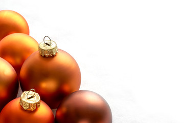Mat bronze orange colored chtristmas balls on a white snowy background for use as a christmas card...