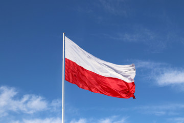 White-red horizontal flag on a flagpole developing in the wind against a blue sky with light clouds. Symbol of the Polish state.