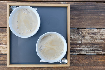 Two cups of milk and coffee in a tray on a wooden table. View from above, tray is on the left.