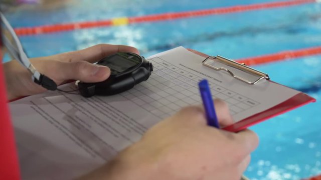 Judge at competition in pool. Close-up of the judge's hand in the pool which records the testimony in the sheet