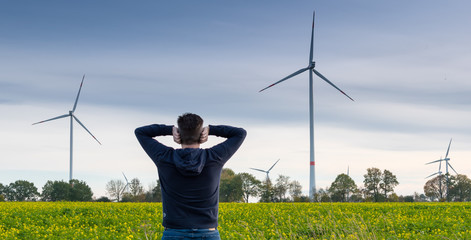 Man infront of a wind farm blocks his ears to reduce the noise