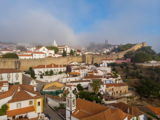 Scenic view of white houses red tiled roofs, and castle from wall of fortress with clouds. Obidos village, Portugal.