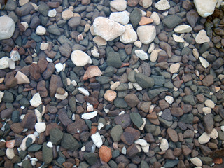 a full frame image of different colored rocks and pebbles in running water and the bottom of a river