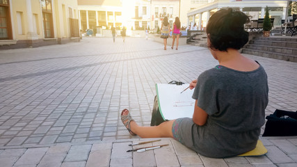 Inspired female street artist sitting on pavement and painting, art and hobby