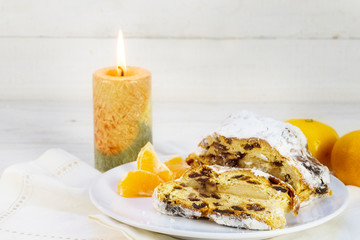 christmas cake, german christstollen with tangerines and a burning candle against a white wooden background with copy space