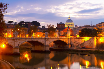 St. Peter's cathedral dome over bridge and river in Rome illuminated at night, Italy