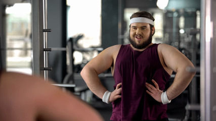 Funny obese man looking at mirror reflection and posing like macho, motivation