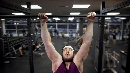 Overweight man trying to pull up on sport bar in gym desire to lose extra weight