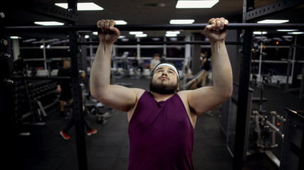 Fototapeta na wymiar Chubby man pulling up on bar, desire to lose weight and be strong, motivation