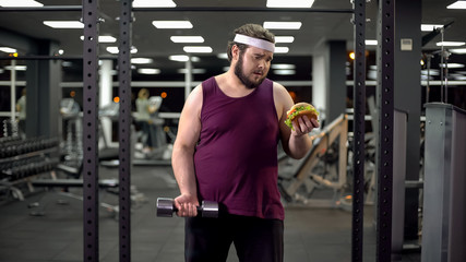 Overweight man holding burger and dumbbell in hands, life decision, motivation