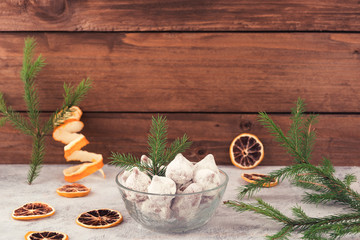 Chocolate candies in white powdered sugar, Christmas decorations-fir branches, dried lemon slices, wooden background.