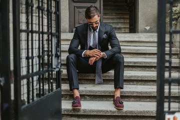 Businessman waiting on the stairs and looking at the time