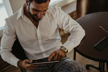 Elegant smiling man looking at the tablet in a cafe