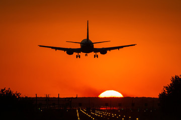 Fototapeta na wymiar Silhouette of air plane landing on illuminated track at sunset with beautiful red sky and sun in background