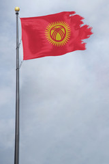 Worn and tattered Kyrgyzstan flag blowing in the wind on a cloudy day