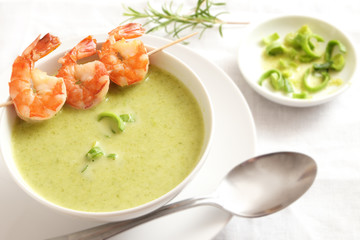 king prawn skewer on green vegetable cream soup, white tableware