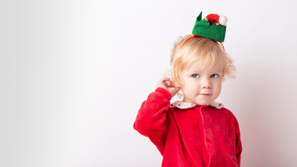 Portrait of cute cute baby girl 1.5 years old, in red clothes And in the cap of the gnome helper Santa.close-up on a white light background. concept christmas