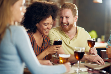 Multicultiral friends sitting in restaurant and drinking wine and beer.