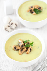 Mushroom cream soup garnished with roasted mushroom slices and parsley, photographed with natural light (Selective Focus, Focus in the middle of the first soup)