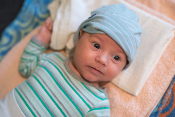 The newborn (2 months baby) with a hat is lying on the bed and laughing