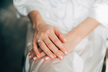 Bride's morning, woman wearing white silk dressing gown, elegant diamond ring on the finger 