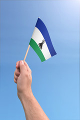 Hand holding Lesotho flag high in the air, with a clear blue sky