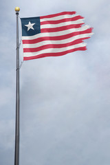 Fototapeta premium Worn and tattered Liberia flag blowing in the wind on a cloudy day