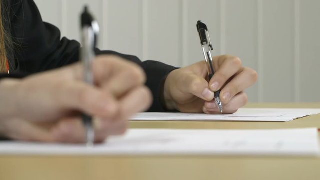 Hands writing in an exam or classroom with defocussed foreground