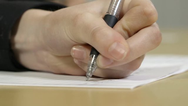 Close up of a hand writing with pen in exam or classroom setting, shallow focus