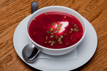 Red Ukrainian borsch with sour cream in a plate is on the table.