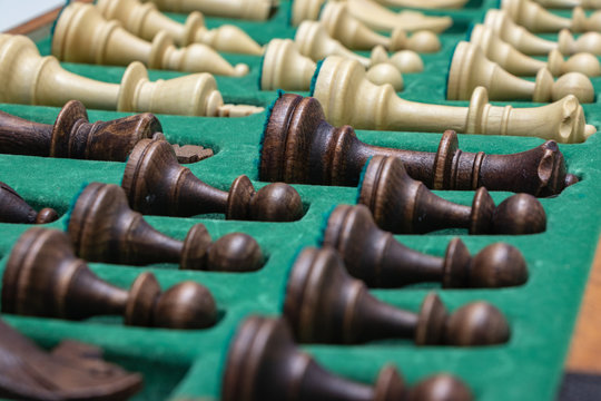 wooden chess pieces (white / black) are neatly folded in a box with a green background