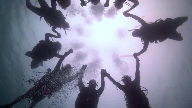 Divers handheld in a big circle with the light of the surface in their back.