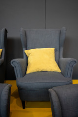 Grey fabric chair with yellow pillow against grey background.
