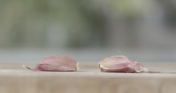 Cloves of garlic being crushed on a wooden chopping board