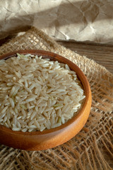 Wood bowl filled with organic long grain rice under low light.