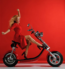 Naklejka na ściany i meble Woman ride new electric car motorcycle bicycle scooter with hands spread freedom sign laughing smiling on red background