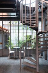 Cozy dining space in natural light scene with small garden in the background and spiral metal stair on foreground / cafe concept / natural light concept / interior design