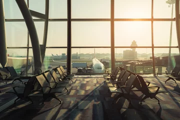 Fotobehang Luchthaven Lege stoelen in de vertrekhal op de luchthaven met vliegtuig dat opstijgt bij zonsondergang. Reizen en vervoer in luchthavenconcepten.