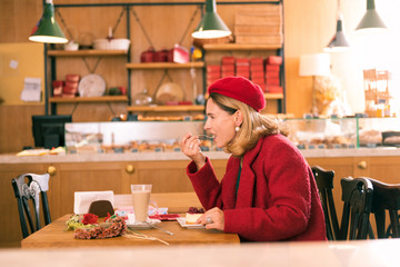 Fruit cheesecake. Fashionable blonde-haired French woman tasting delicious fruit cheesecake in her favorite bakery