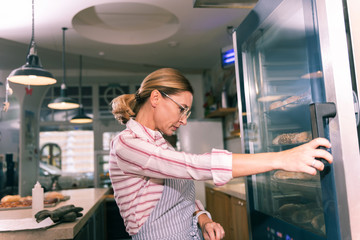 Fridge with desserts. Owner of French bakery wearing glasses looking at fridge with desserts before calling suppliers