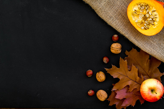 Composition with autumn vegetables and leaves in red and orange colors. Brown dried leaves, pumpkin, apple on black background top view copy space