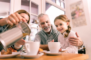 Morning tea. Beautiful cute dark-eyed granddaughter drinking tea in the morning with grandparents