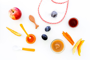 Ingredients for baby puree. Assortment of flavors of baby food. Vegetables and fruits. Apple, carrot, pumpkin, prune near bib on white background top view