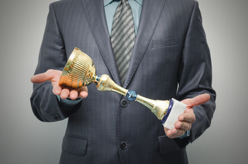 Businessman is holding a golden award trophy in the hands isolated on gray background.