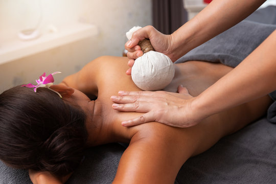 Asian woman enjoying compress balls, herbal ball massage at spa.