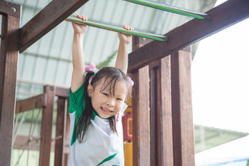 Little asian girl hanging bar in school playground