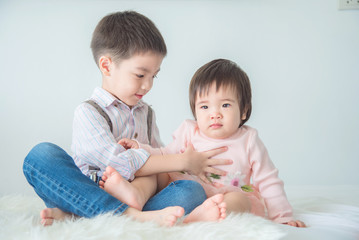 Little asian brother sitting with his sister on bed at home