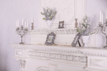 Shiny white candles decorated place for photo made by old white fireplace.Winter design,scandinavian style .Living room with fire place.candles and silver candlestick.Vintage decoration.