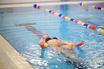 Pregnant woman with foam roller in the pool